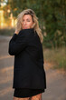 © shymar27 - Confident woman with wavy blonde hair wearing a black blazer stands outdoors, showcasing a relaxed yet professional demeanor in a natural setting