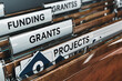 © Pixel Studio - Closeup of file folders labeled funding grants grantss and projects in an office setting showcasing organization and management of financial resources and project documentation for business use