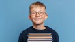 © Julia - The boy, who is wearing glasses and a yellow sweater, has a stack of books in his hands and a smile of happiness