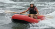 © Daniel L - A woman white water rafting in a red raft. Helmet and life jacket. Fearful but confident expression. Water sport.