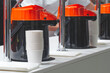© Aleksandr Matveev - A coffee dispenser with a white cup next to it. There are many white cups on the counter