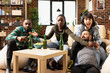 © DC Studio - African American man and Caucasian woman compete in video game with wireless controllers while friends watch. Diverse group laughing, bonding and enjoying relaxed hangout in cozy living room.