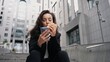 © Vlad - Caucasian girl with brown long hair sitting on stairs downtown talking by phone and eating delicious hamburger. Outdoor, smartphone, food.