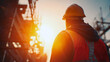 © AS Studio - Silhouette of a construction worker in a hard hat and safety vest against a bright sun flare