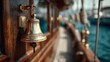 © Oulaphone - A close-up of a brass ship's bell attached to wooden decking, with a blurred background of boats and water, evoking a nautical atmosphere.