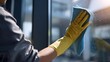 © Julian - Close-up of a cleaner's hand in a yellow glove wiping a glass window with a blue cloth in a modern office