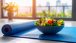 © NikProArt - A vibrant salad in a blue bowl rests on a blue yoga mat, bathed in warm sunlight streaming through a window.