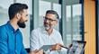 © sajed - Two businessmen collaborating and discussing ideas while looking at a tablet computer in an office setting