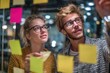 © ttonaorh - Group of young professionals collaborating during brainstorming session, using colorful sticky notes on glass wall in modern office.