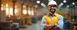 © Vadym - Confident indian man smiles with crossed arms in factory. Engineer wears helmet, uniform, orange vest. Positive employee stands in manufacturing shop at facility. Supervisor at metal production