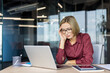 © Liubomir - Stressed businesswoman suffering from a headache while working intently on a laptop in a modern office, depicting concepts of burnout and work-life imbalance