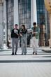 © qunica.com - Three people walk outside a glass-fronted building, examining documents and brochures as they discuss ideas.