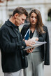 © qunica.com - A man and woman in smart attire examine papers and notebooks outside, discussing information and coordinating tasks.