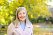 © Liubomir - Senior woman enjoying a beautiful autumn day in the park. Featuring a confident and happy expression. Wearing a warm coat. And standing confidently against a blurred background of vibrant yellow trees