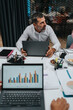 © qunica.com - A focused man sits at a conference table with a laptop, surrounded by charts, documents, and snacks. The scene captures teamwork, data discussion, and strategic planning in a corporate setting.
