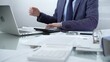 © volha_r - Businessman wearing blue suit is working with laptop while sitting and gesturing with his hands at the glass table in office background. Low lighting, close-up view. Business people and audit concept