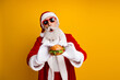 © deagreez - Santa Claus holding a festive burger in cheerful Christmas attire, standing in front of a vibrant yellow background.