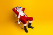 © deagreez - Cheerful Santa Claus relaxing in a deck chair against a vibrant yellow background, enjoying a fun and festive holiday moment