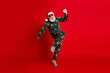 © deagreez - Funny santa in christmas pajama jumps against red background wearing sunglass for holiday party mood and festive dream