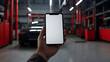 © photo for everything - Close-up on a person holding a smartphone with a blank screen inside an auto repair shop, with a car lift in the background, ideal for showcasing mobile apps in the auto industry.