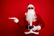 © deagreez - Santa Claus in a red suit with belt and beard poses with sunglass red background for Christmas holiday shopping and festive season promotion