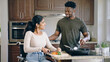 © Eduardo Accorinti - Happy interracial couple looking at each other while cooking together in the kitchen, with the woman in a wheelchair