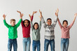 © Prostock-studio - A group of preteen kids stand together with their hands raised in joy. They are smiling widely, celebrating their achievements against a simple gray background.