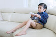 © Creativa Images - Cute Asian Boy Holding a Remote Control and Snack Bowl while Watching TV on a White Sofa