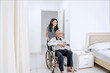 © Creativa Images - Young Female Caregiver Pushing Elderly Man in Wheelchair in Bright Home Setting