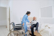© Creativa Images - Female nurse helping senior male patient sit on a bed beside a wheelchair in a bright room.