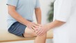 © grooveisintheheart - A male patient with leg pain is receiving physical therapy from the nurse. A patient is sitting on the examination table and holding their knee with both hands while being examined
