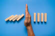 © Dadan - male hand stop falling wooden blocks isolated on blue background. domino effect or risk protection strategy concept