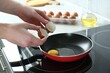 © New Africa - Woman cracking egg into frying pan in kitchen, closeup