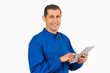 © cunaplus - Confident smiling professional handyman in blue overalls using digital tablet with white background.