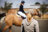 Horse trainer closely monitoring rider preparing for dressage event. Horseback riding in equestrian paddock