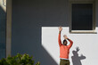 © TrueFrame Collective - African American man  standing outdoors raising arms toward sunlight casting distinct shadow on wall background, facial expression showing excitement and engagement