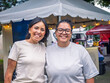 © SALMONNEGRO - Portrait of a lesbian couple of entrepreneurial women in front of their street michelada stand, smiling and tending to their business.