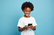 © Maryna - Happy kid with curly hair uses smartphone. Smiling boy holding cellphone isolated on blue background. Child enjoys mobile app. Tech fun connection concept. Modern communication