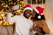 © Prostock-studio - Happy young black couple celebrates New Year in a cozy room decorated for the holidays. She kisses him while he takes a selfie. They drink from glasses filled with festive cheer.