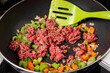 © SockaGPhoto - A skillet frying pan of ground beef with celery and carrot pieces with a spatula stirring