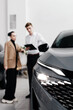 © wedmoments.stock - Professional car dealership scene featuring a woman discussing vehicle features with a salesman, showcasing modern automotive design and customer engagement in a sleek showroom environment
