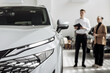 © wedmoments.stock - White SUV showcased in a modern car dealership, with a male salesperson discussing features with a female customer, highlighting the car sales experience and customer service