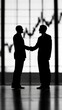 © Yuparet - Silhouette of Two Business Professionals Shaking Hands Against a Skyline with Graphs Symbolizing Growth and Collaboration in a Corporate Environment