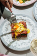 © Pietro Karras/Stocksy - Cutting into eggs benedict on toast with runny yolk