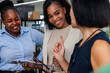© Jovo Jovanovic/Stocksy - Three women collaborate, smiling, discussing documents on a clipboard.