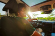 © BONNINSTUDIO/Stocksy - Man driving car and smiling at sunset with sun flare