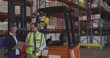 © vectorfusionart - Reviewing two staff in safety vest comparing inventory in storage bay, with forklift, copy space