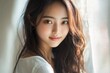© Imagehub - A beautiful young Asian woman with long wavy hair, softly smiling, gazing gently at the viewer in natural light. Her features are delicate and serene.