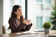 © wattana - Thoughtful businesswoman sitting at desk, holding a pen and reflecting during a meeting.