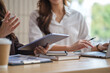 © wattana - Close-up of female colleagues discussing business data using a tablet, laptop, and documents during a meeting.